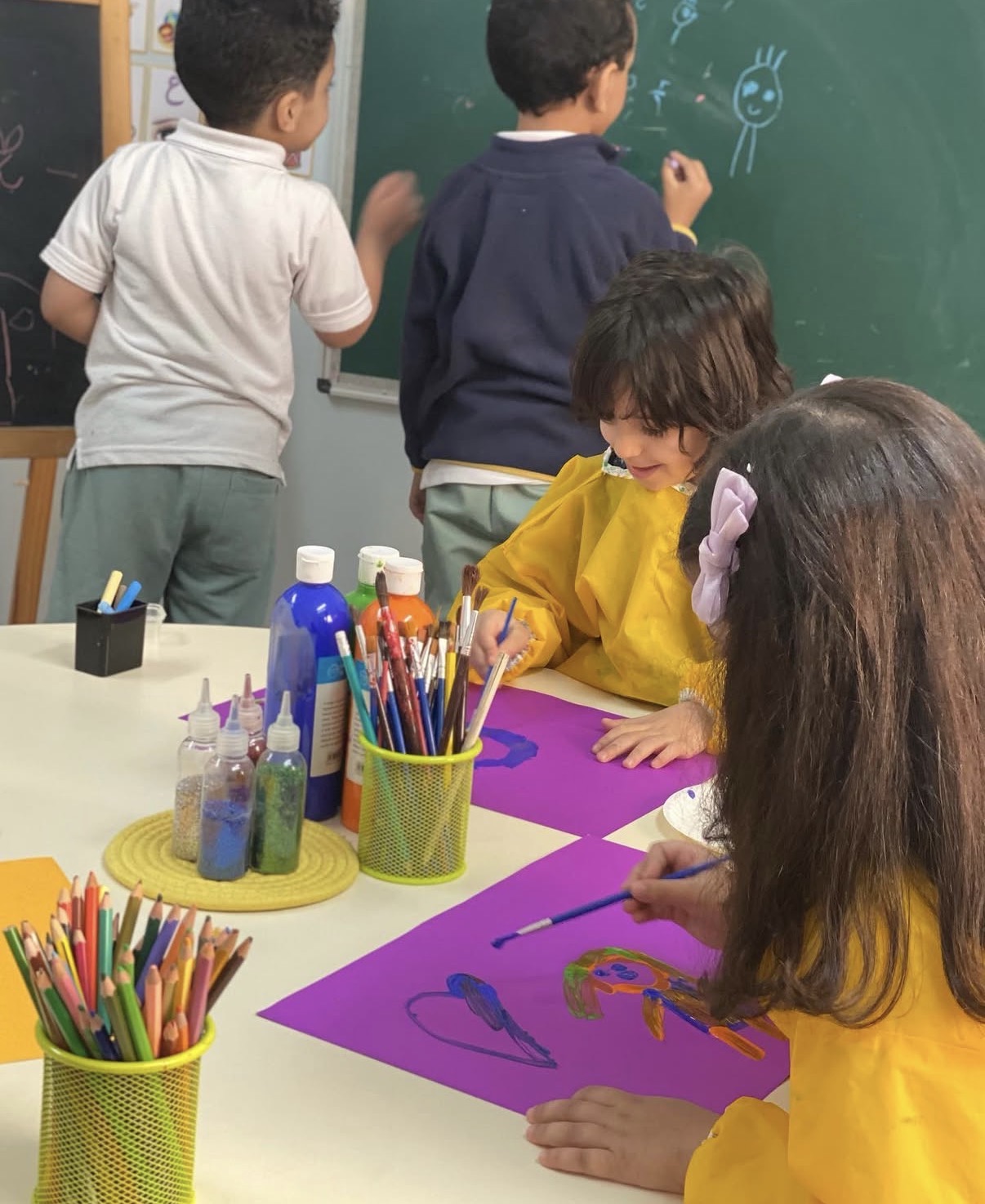 أطفال يرسمون بالألوان على طاولة الأنشطة داخل فصل كيدز تايم